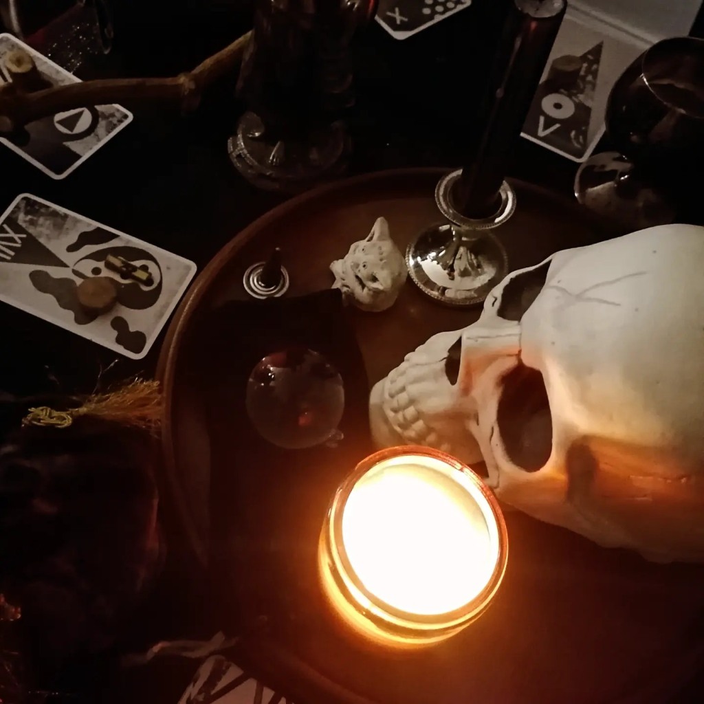 Candlelit altar from above with black and white tarot cards, small crystal ball, fake skull, goblet and gremlin